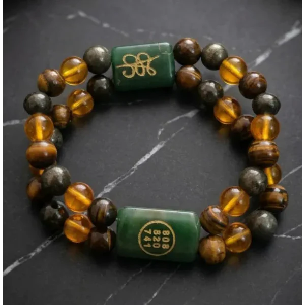 A beaded bracelet with alternating translucent amber and dark brown beads, accented by two green cylindrical charms with gold Chinese characters, displayed on a dark slate surface.