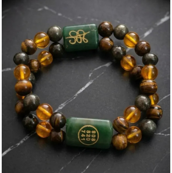 A beaded bracelet with alternating translucent amber and dark brown beads, accented by two green cylindrical charms with gold Chinese characters, displayed on a dark slate surface.